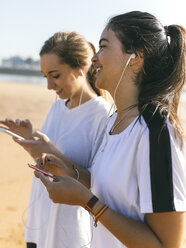 Spanien, Gijon, zwei sportliche junge Frauen mit Ohrstöpseln am Strand - MGOF000214