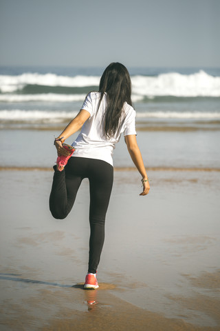 Spanien, Gijon, junge Frau streckt sich am Strand, lizenzfreies Stockfoto