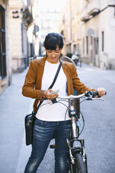 Spanien, Barcelona, lächelnde Frau mit Fahrrad und Mobiltelefon in der Stadt - EBSF000585
