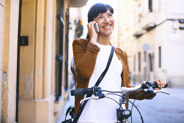 Spain, Barcelona, smiling woman with bicycle and cell phone in the city - EBSF000581