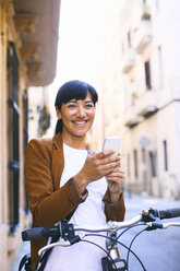 Spanien, Barcelona, lächelnde Frau mit Fahrrad und Mobiltelefon in der Stadt - EBSF000586