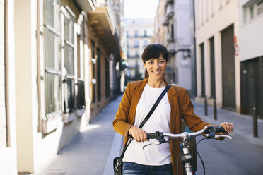 Spain, Barcelona, smiling woman with bicycle in the city - EBSF000582