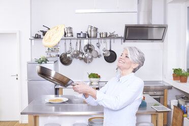 Reife Frau in der Küche, die einen Pfannkuchen in die Pfanne wirft - FMKF001448