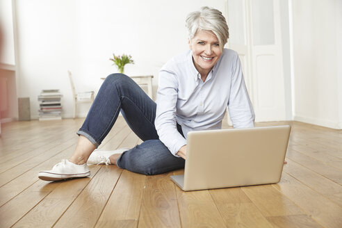 Reife Frau sitzt auf dem Boden und benutzt einen Laptop - FMKF001454