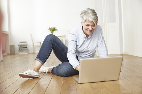 Reife Frau sitzt auf dem Boden und benutzt einen Laptop - FMKF001455