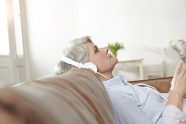Mature woman sitting on couch listening to music - FMKF001466