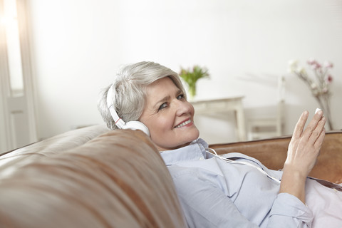 Reife Frau sitzt auf der Couch und hört Musik, lizenzfreies Stockfoto