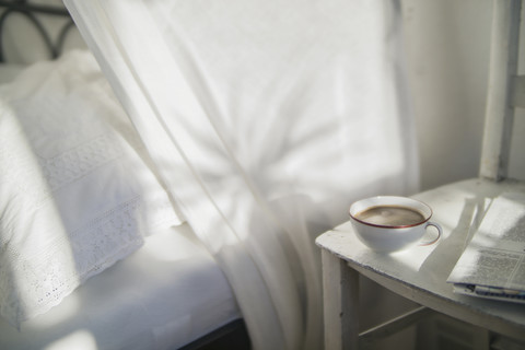 Tasse Kaffee und Zeitung auf einem alten Stuhl im Schlafzimmer, lizenzfreies Stockfoto