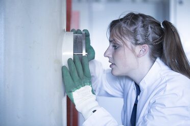 Junge Frau im Laborkittel schaut durch ein Guckloch - SGF001544