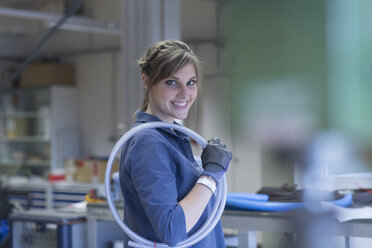 Technician in workshop carrying hose - SGF001559