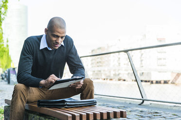 Man sitting on bench using digital tablet - UUF004015