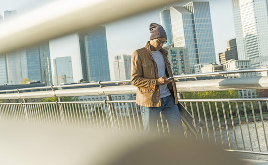 Deutschland, Frankfurt, Mann auf Brücke mit Skateboard schaut auf Smartphone - UUF004033
