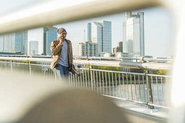 Deutschland, Frankfurt, Mann auf Brücke mit Skateboard spricht mit Smartphone - UUF004034