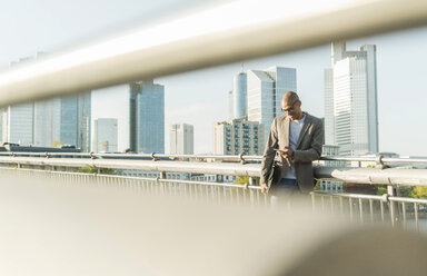 Germany, Frankfurt, businessman on bridge looking on smartphone - UUF004035