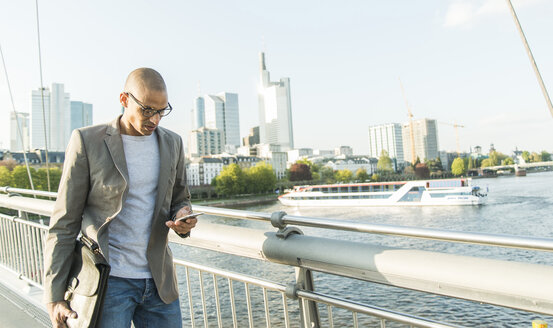 Deutschland, Frankfurt, Geschäftsmann auf Brücke schaut auf Smartphone - UUF004037