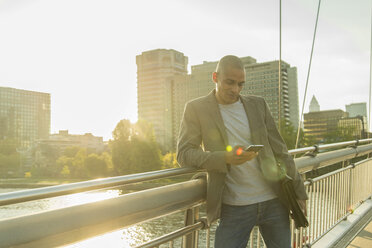 Deutschland, Frankfurt, Geschäftsmann auf Brücke schaut auf Smartphone - UUF004043