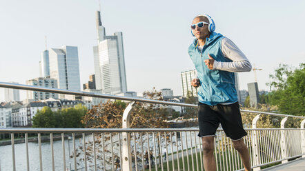 Deutschland, Frankfurt, Mann mit Kopfhörern joggt auf Brücke - UUF004048