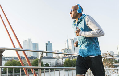 Germany, Frankfurt, man wearing headphones jogging on bridge - UUF004078