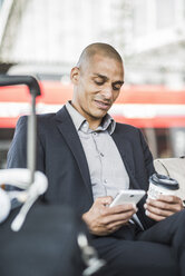 Businessman at the train station looking on smartphone - UUF004056