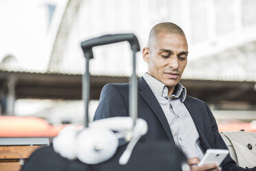 Geschäftsmann auf dem Bahnhof schaut auf sein Smartphone - UUF004057