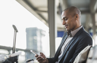 Geschäftsmann auf dem Bahnhof schaut auf sein Smartphone - UUF004059