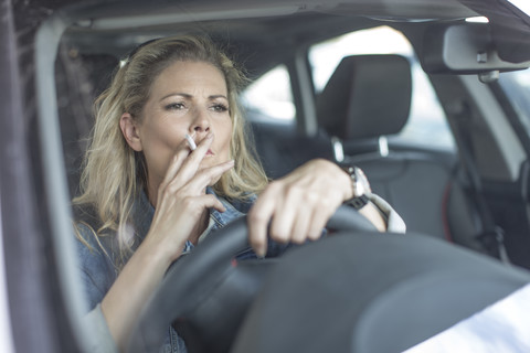 Ernste Frau im Auto raucht eine Zigarette, lizenzfreies Stockfoto