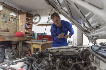 Mann arbeitet an einem Auto in der heimischen Garage und schaut auf den Ölmessstab - ZEF004813