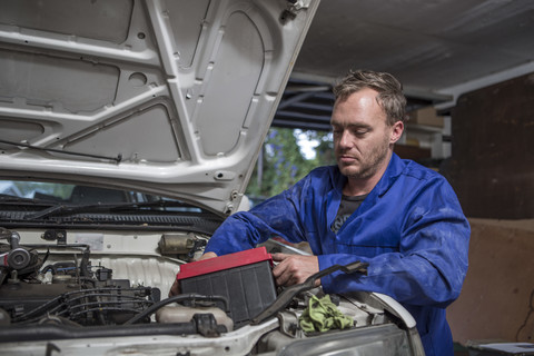 Mann arbeitet in der heimischen Garage am Auto und baut die Batterie aus, lizenzfreies Stockfoto