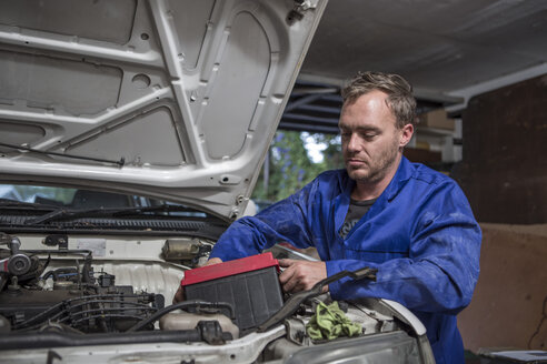 Mann arbeitet in der heimischen Garage am Auto und baut die Batterie aus - ZEF004817