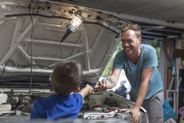 Son helping father in home garage working on car - ZEF004823