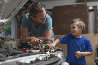 Son helping father in home garage working on car - ZEF004825