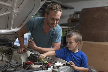 Son helping father in home garage working on car - ZEF004826