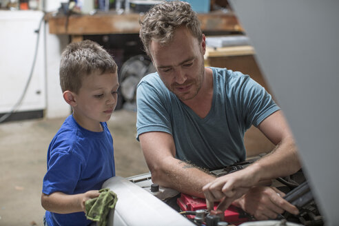 Son helping father in home garage working on car - ZEF004827