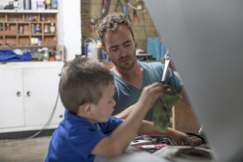 Son helping father in home garage working on car - ZEF004878