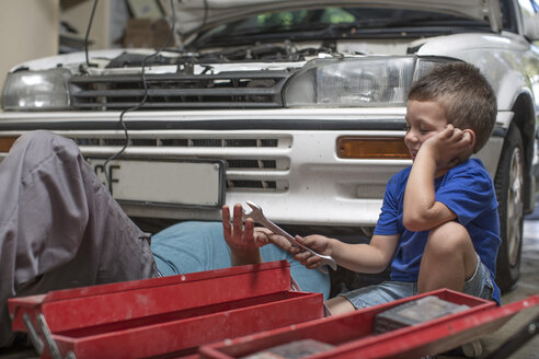 Son helping father in home garage working on car - ZEF004880