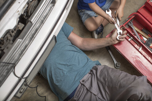 Son helping father in home garage working on car - ZEF004829