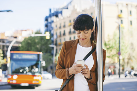 Spain, Barcelona, businesswoman with smartphone waiting at the bus stop stock photo