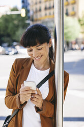 Spain, Barcelona, businesswoman with smartphone waiting at the bus stop - EBSF000591