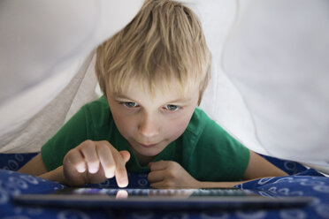 Boy using digital tablet in bed under blanket - PDF000930