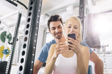 Junges Paar mit Smartphone nach dem Training im Fitnessstudio - MADF000213