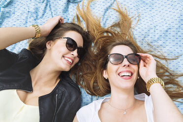 Two laughing women with sunglasses lying on blue sarong - GEMF000240