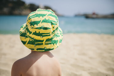 Spain, Mallorca, Porto Christo, back view of little boy sitting on the beach wearing summer hat - MFF001587