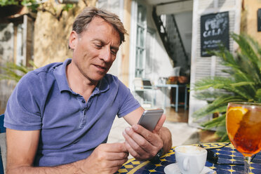 Spain, Mallorca, Arta, portrait of man sitting at courtyard of a cafe using smartphone - MFF001598