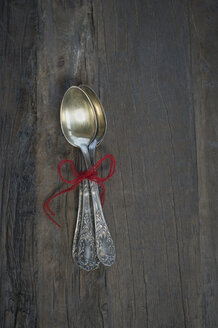 Old silver spoons tied together with red thread on dark wood - CRF002683