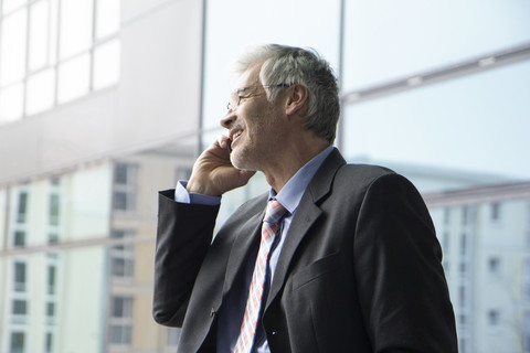 Geschäftsmann steht am Fenster und benutzt ein Mobiltelefon, lizenzfreies Stockfoto