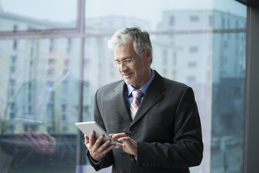 Businessman standing at window using digital tablet - RBF002664