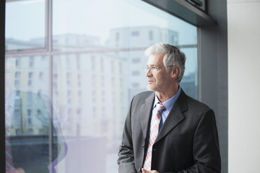 Businessman standing at window looking at distance - RBF002668