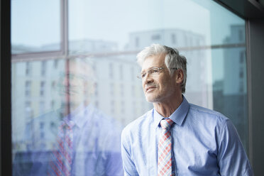 Businessman standing at window looking at distance - RBF002670
