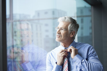 Businessman standing at window looking at distance - RBF002671