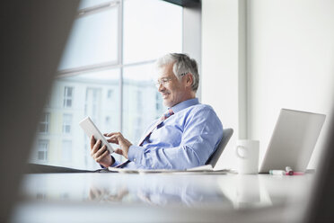 Businessman sitting at , using digital tablet - RBF002743